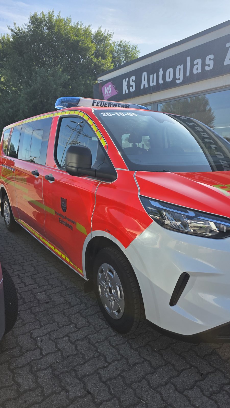 Rotes Einsatzfahrzeug der Freiwilligen Feuerwehr Elmshorn mit Blaulicht auf dem Dach seitlich geparkt