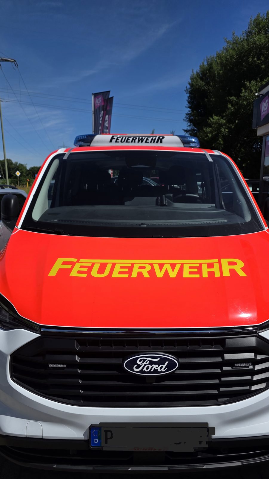 Frontansicht eines roten Feuerwehr-Einsatzfahrzeugs mit Schriftzug auf der Motorhaube und Blaulicht auf dem Dach